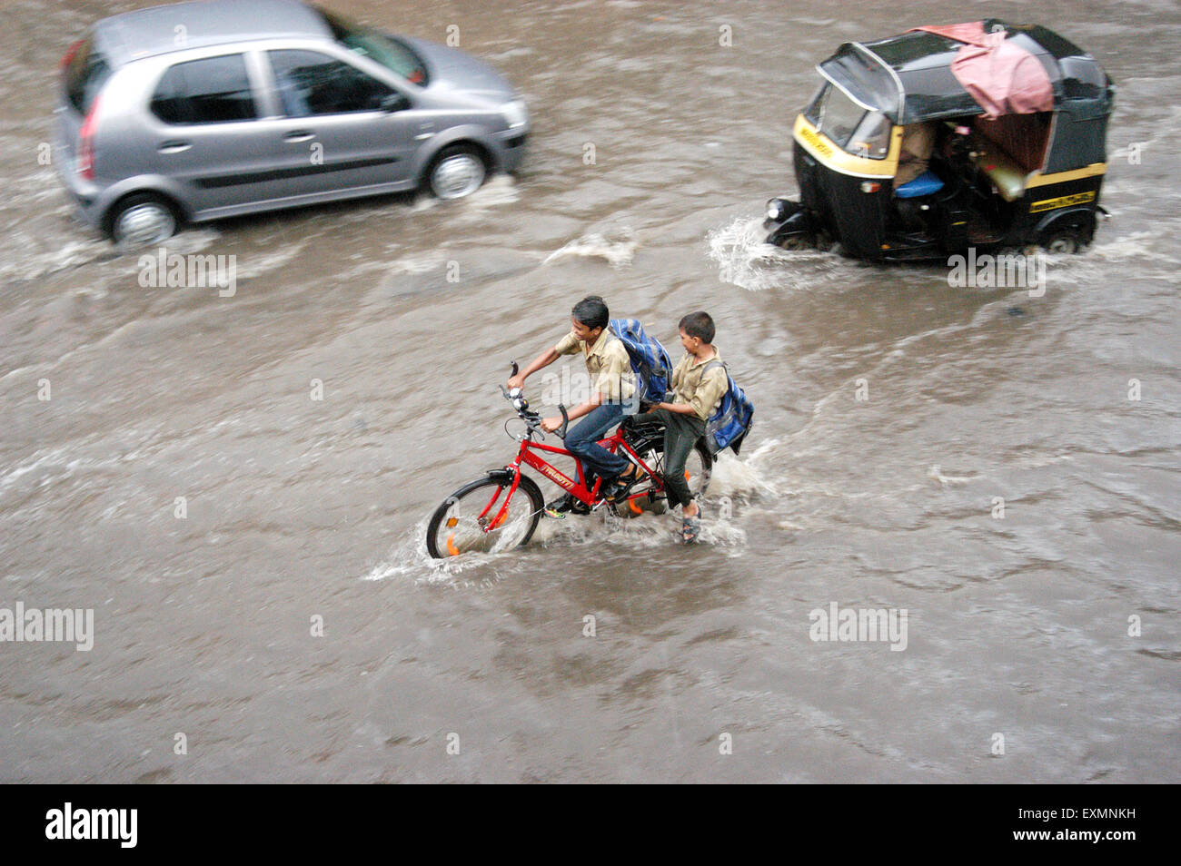 I ragazzi della scuola del ciclo automatico di biciclette risciò piogge monsoniche car guida l'acqua ha invaso street Vidyavihar Mumbai India Foto Stock