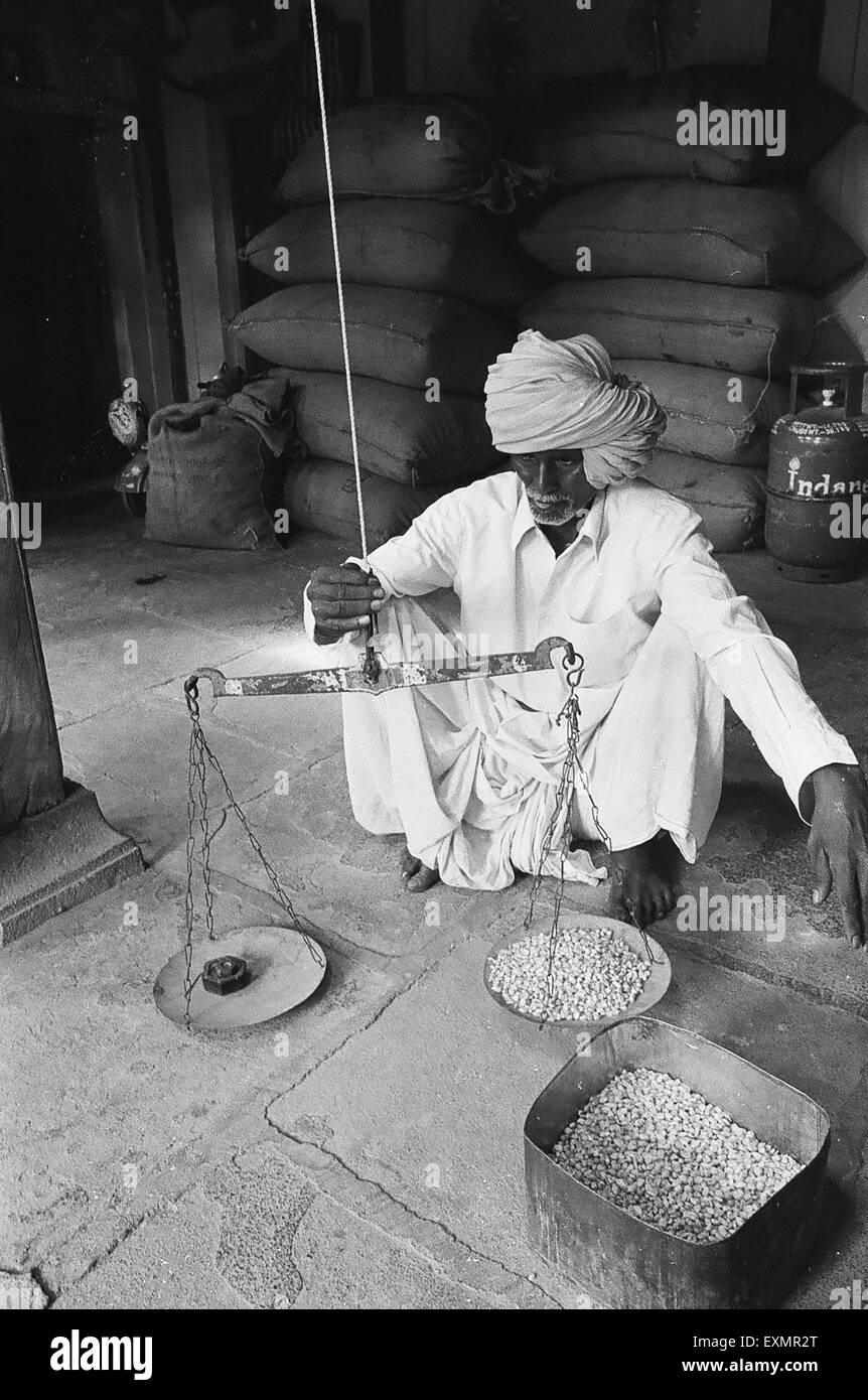Il vecchio uomo di grano di ponderazione in peso in scala Munagli nel distretto di Bijapur del Karnataka ; India Foto Stock