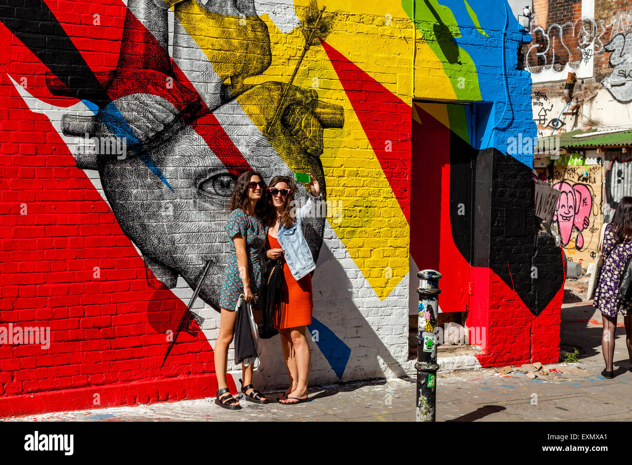 Giovani donne posano per una selfie di fronte a qualche Arte di strada/Graffiti, Brick Lane, Londra, Inghilterra Foto Stock