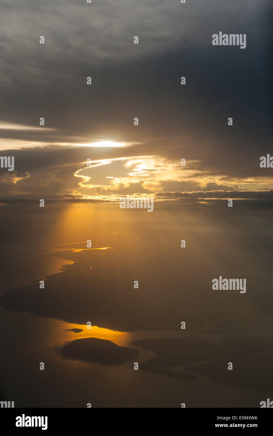 Raggi di sole shininhg sotto un cielo nuvoloso luce di colata sulla terra e fiume sottostante. Foto Stock