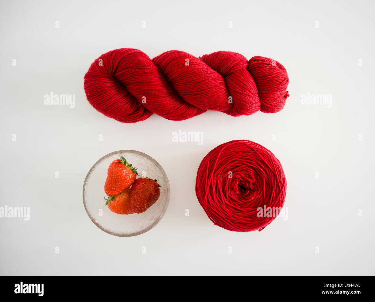 Mano tinto filo rosso e ciotola di vetro di fragole su sfondo bianco Foto Stock