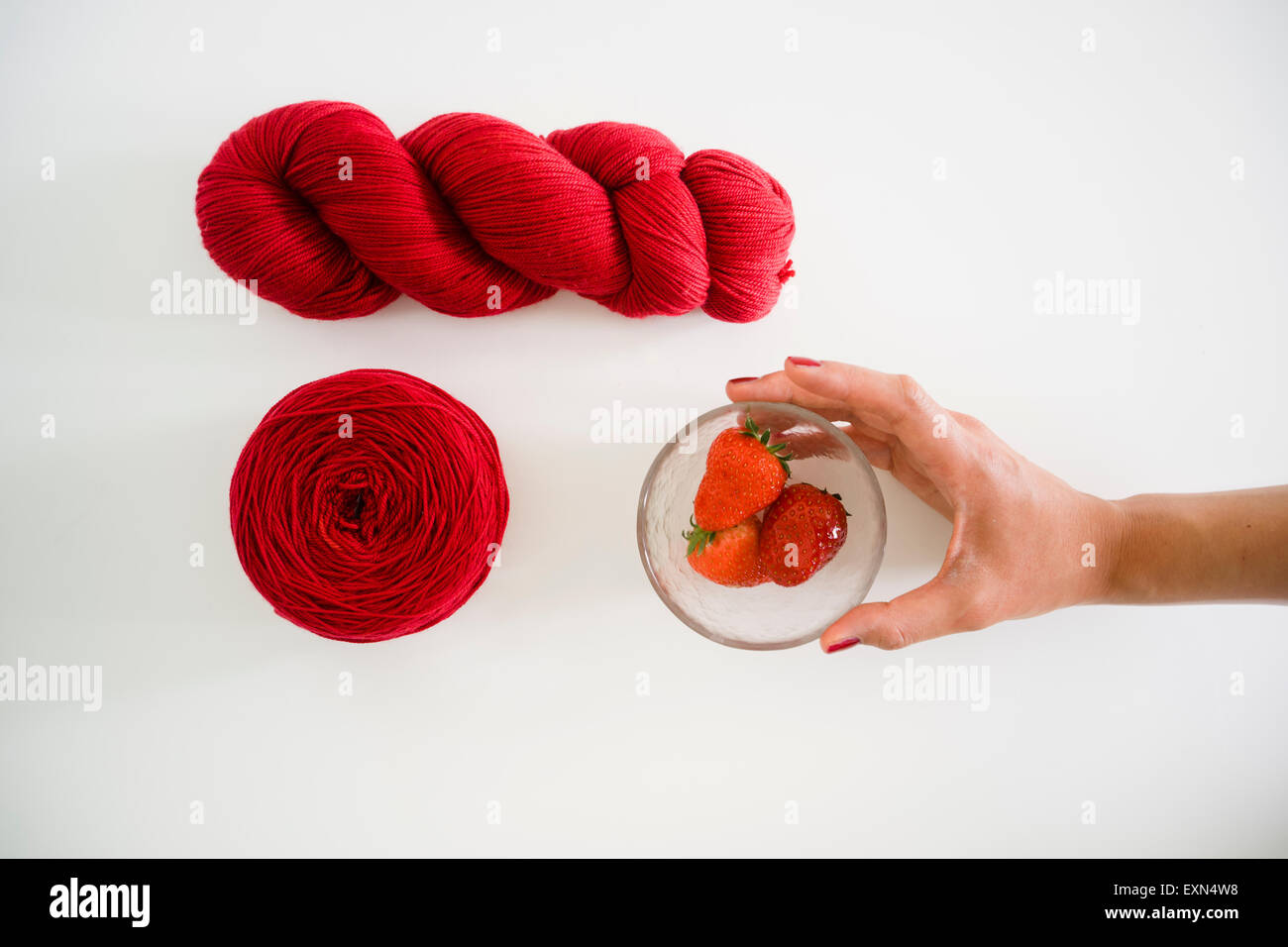 Mano tinto filo rosso e di una donna mano raggiungendo per la ciotola di vetro di fragole Foto Stock