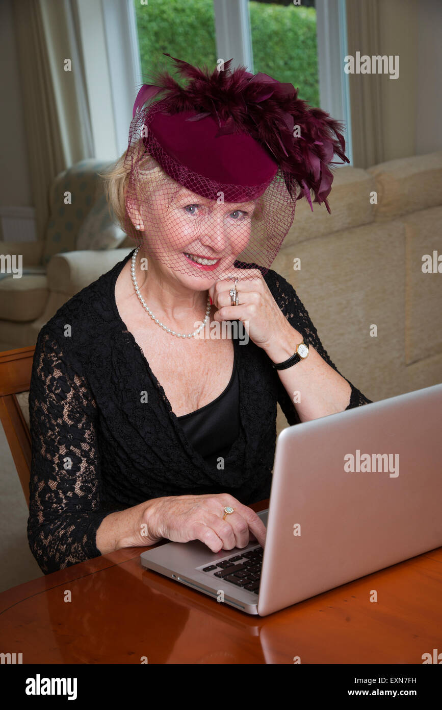 Donna anziana indossando un cappello con piume usando un computer portatile Foto Stock