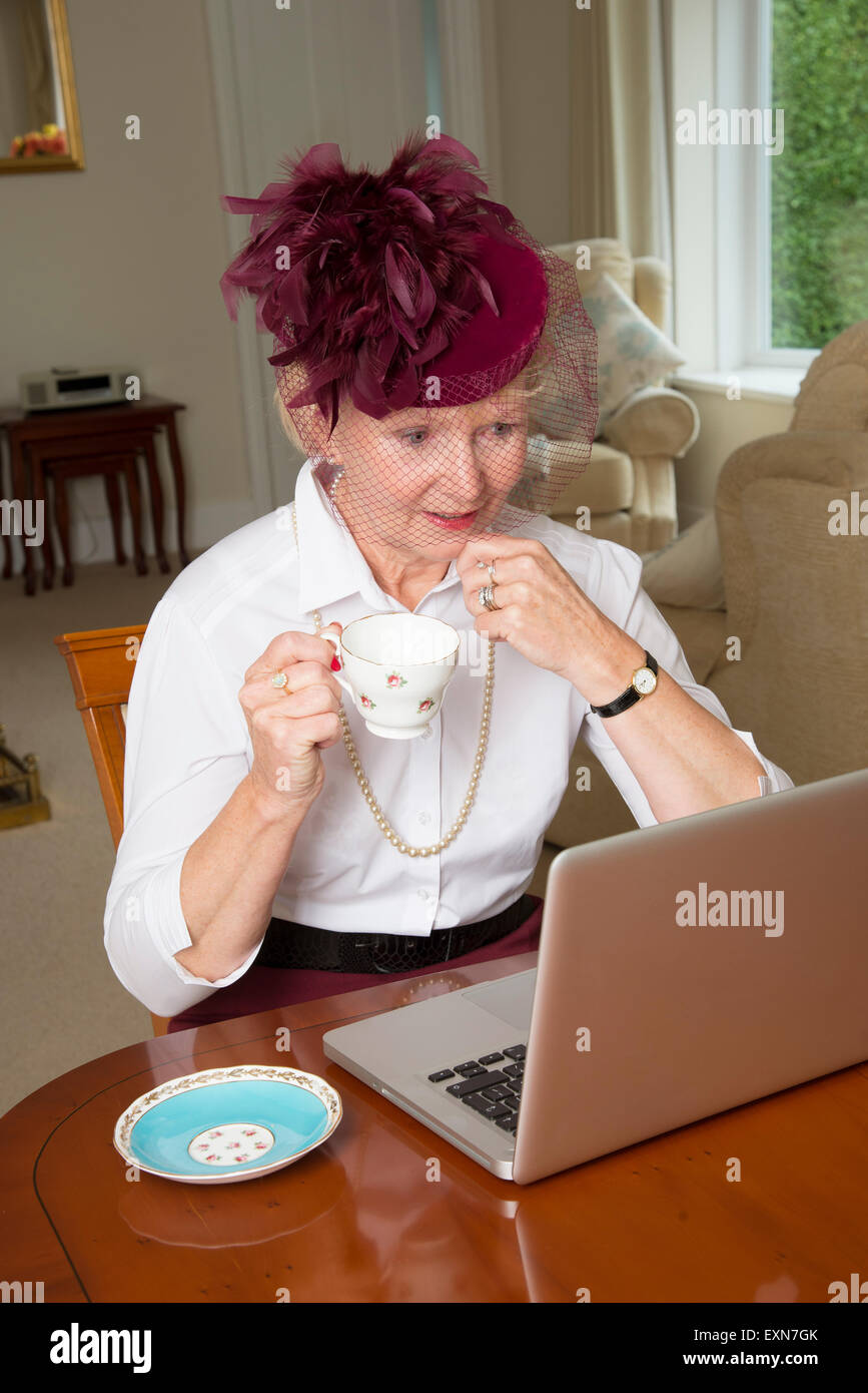 Donna anziana indossando un cappello con piume usando un computer portatile Foto Stock