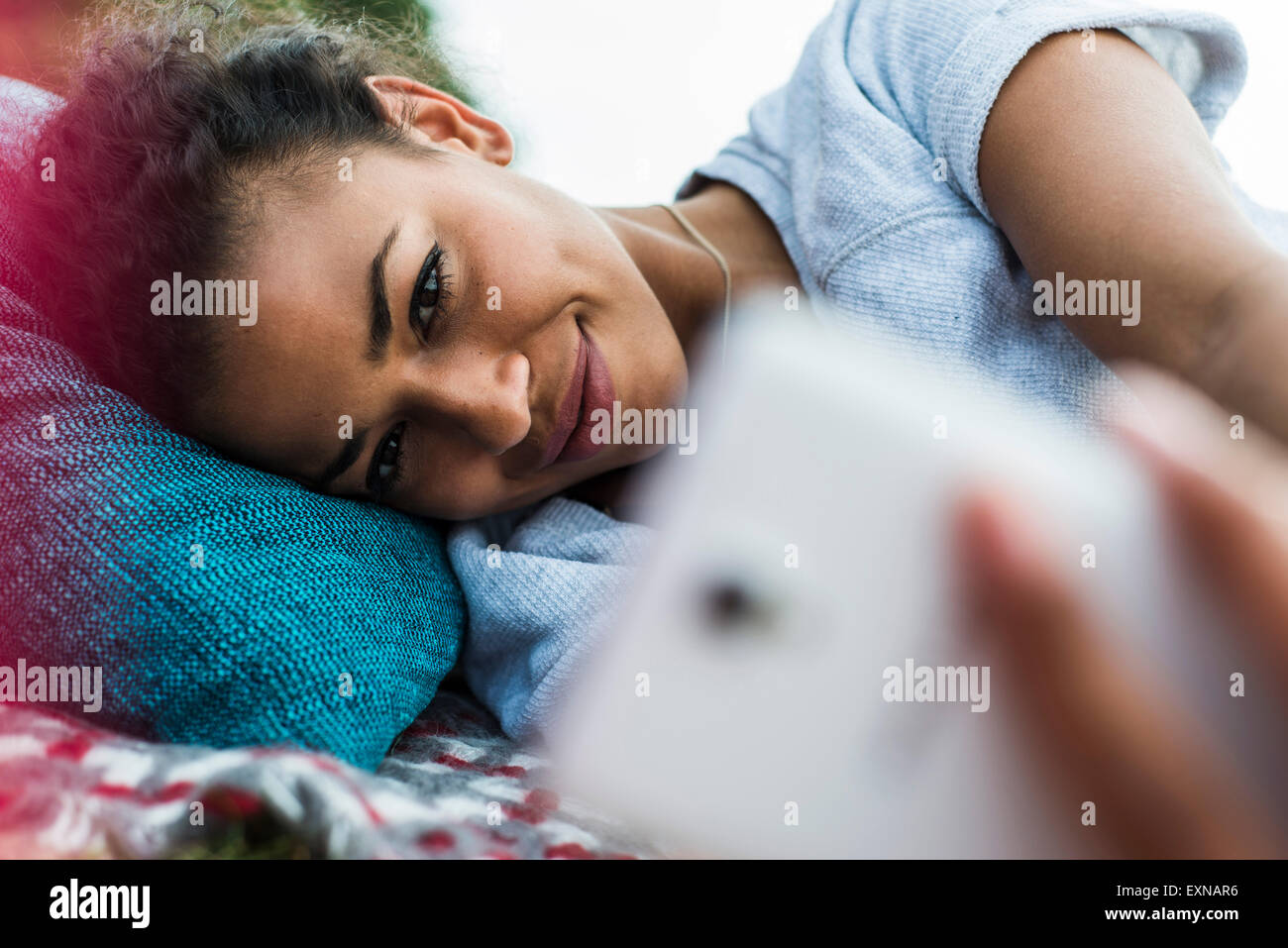Giovane donna giacente all'aperto in possesso di un telefono cellulare Foto Stock