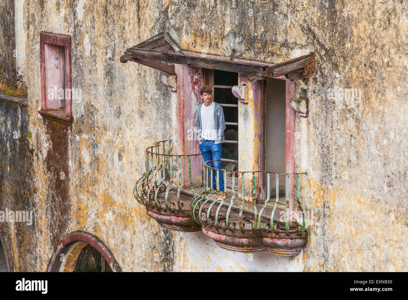 La Grecia, Rodi, Eleousa, giovane uomo in piedi sul balcone di una vecchia casa, rovina dall occupazione italiana periodo Foto Stock