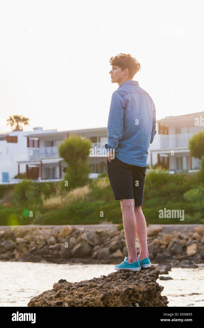 La Grecia, Rodi, giovane uomo in piedi su una roccia sul lungomare guardando a distanza Foto Stock