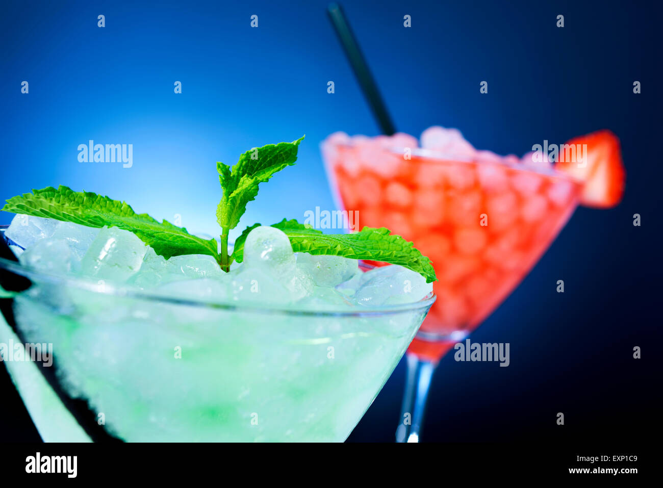 Primo piano di alcuni bicchieri da cocktail con bevande di diversi colori guarnite con foglie di menta e una fragola oltre un paglierino blu Foto Stock