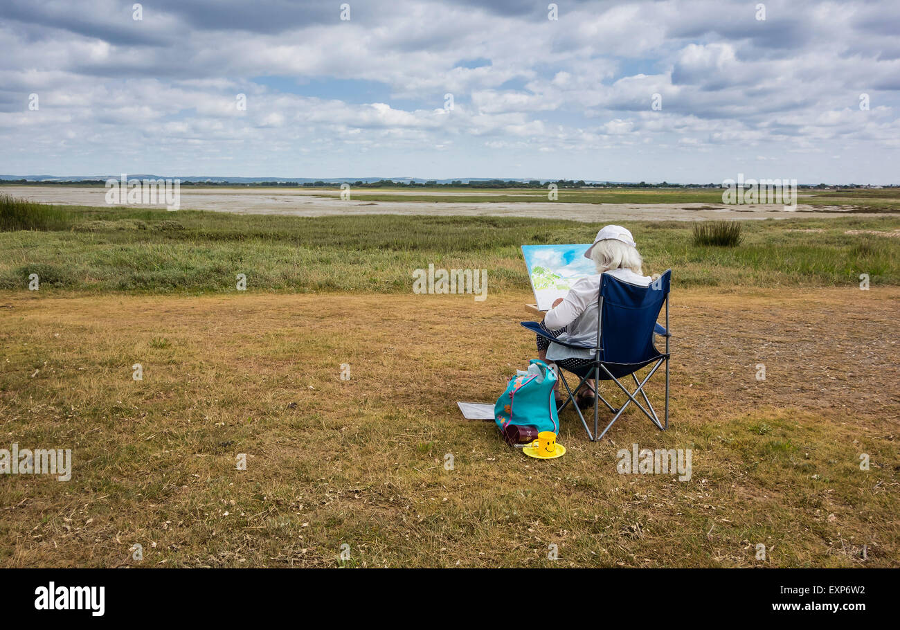 Artista seduto dipinto il paesaggio a Pagham Harbour, West Sussex, in Inghilterra, Regno Unito Foto Stock