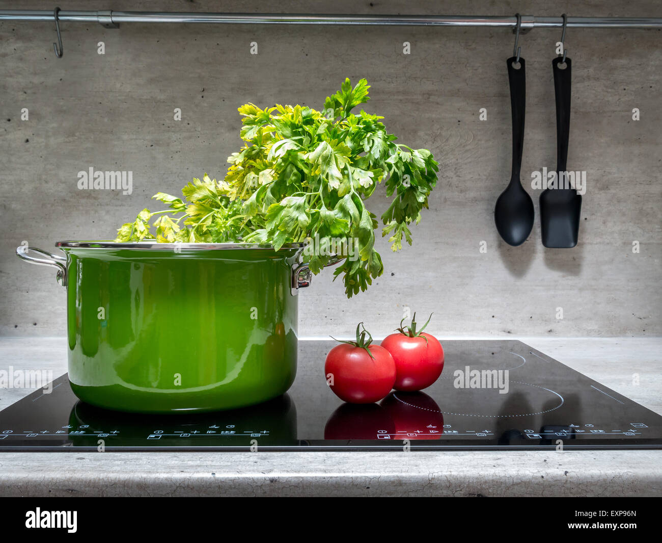 Smalto verde stewpot con prezzemolo e due pomodori nero sul fornello ad induzione Foto Stock
