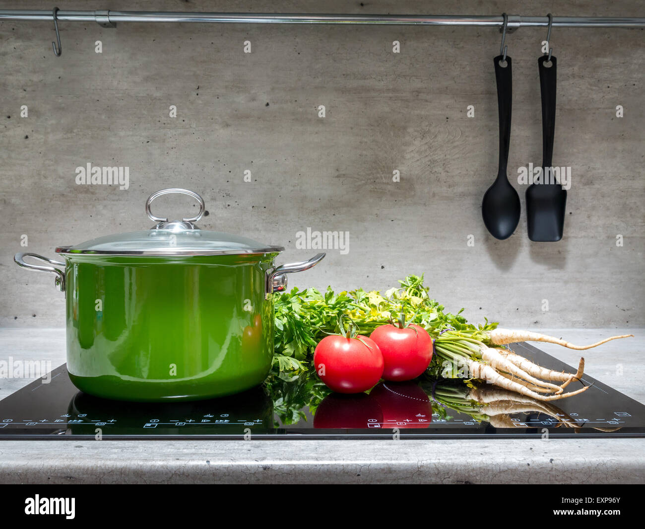 Smalto verde stewpot con prezzemolo e due pomodori nero sul fornello ad induzione Foto Stock