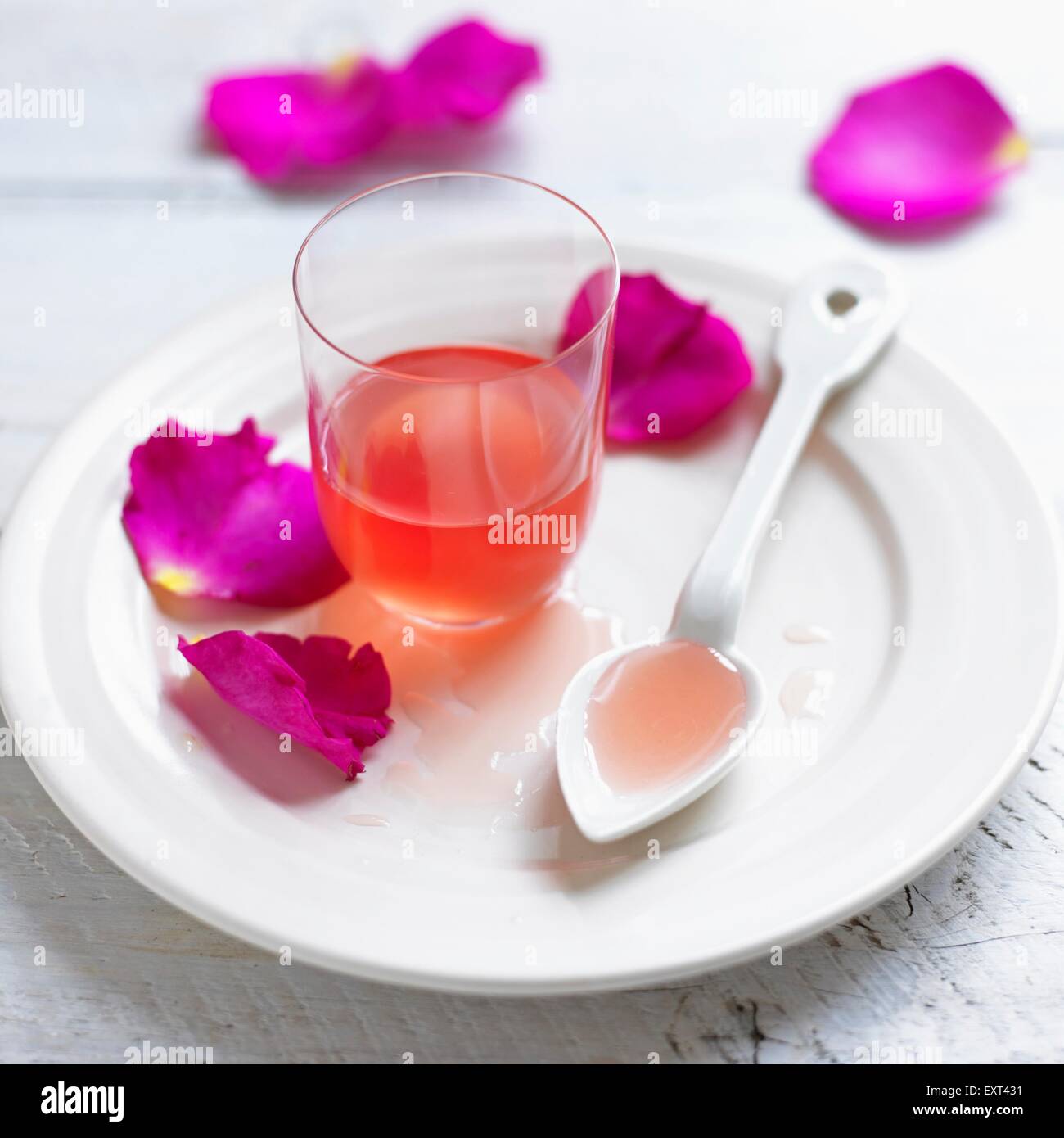 Bicchiere di petali di rose sciroppo con cucchiaio e petali su una piastra Foto Stock