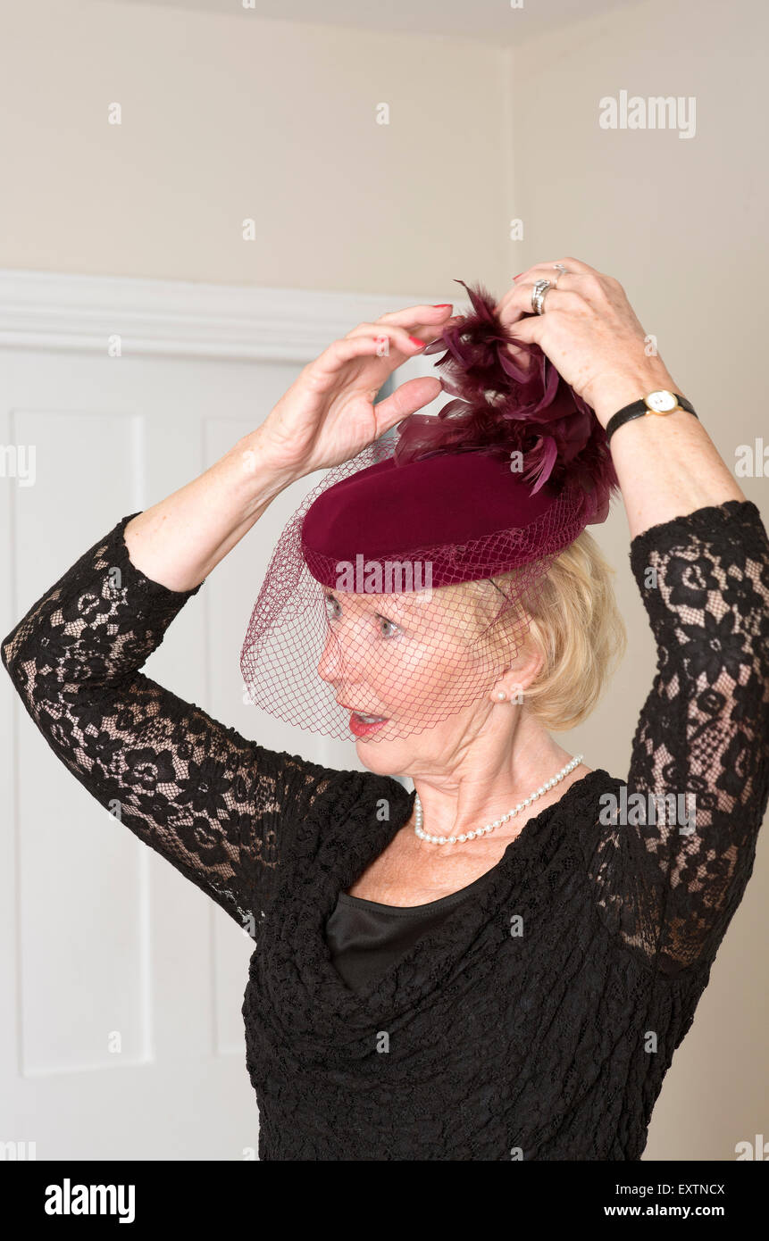 Donna anziana regolando il suo colore marrone cappello e il Velo con piume Foto Stock