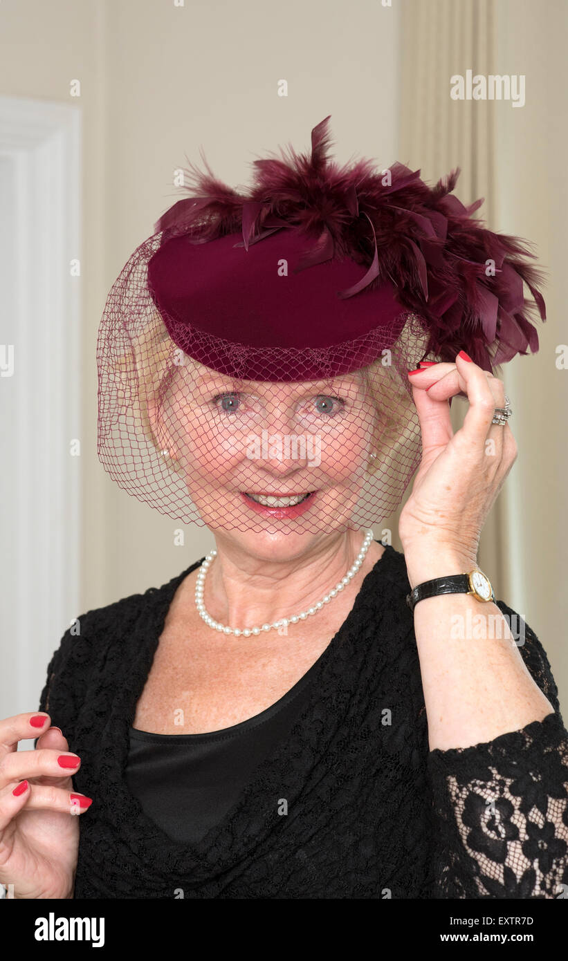Donna anziana regolando il suo colore marrone cappello e il Velo con piume Foto Stock