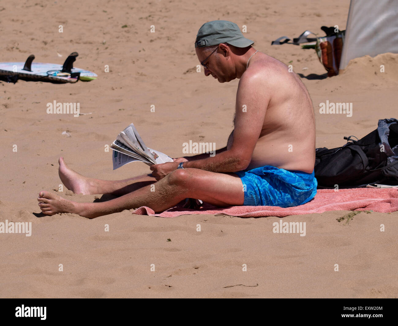 Uomo seduto sulla spiaggia leggendo un giornale, Woolacombe, Devon, Regno Unito Foto Stock