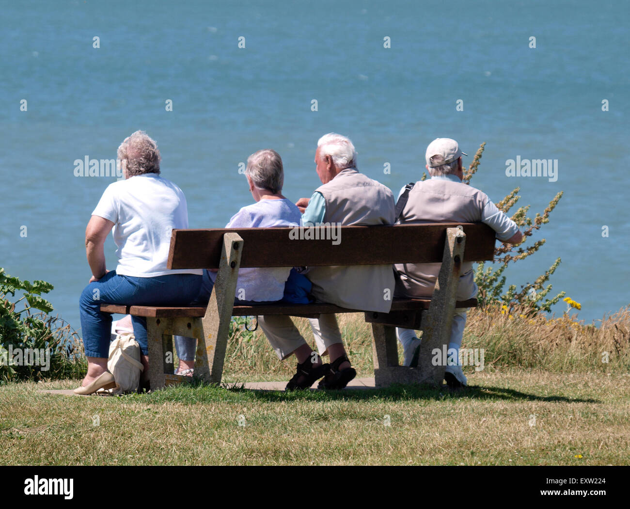 I pensionati seduto su una panchina pubblica che guarda al mare, Woolacombe, Devon, Regno Unito Foto Stock