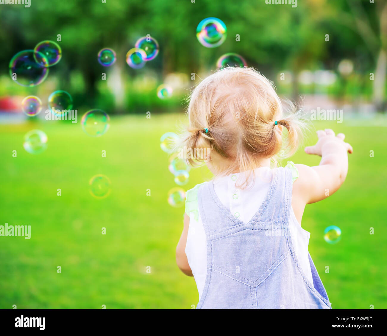 Little Baby girl cercare di cattura bolle di sapone, avendo divertimento all'aperto, giocare nel parco, felice infanzia spensierata Foto Stock