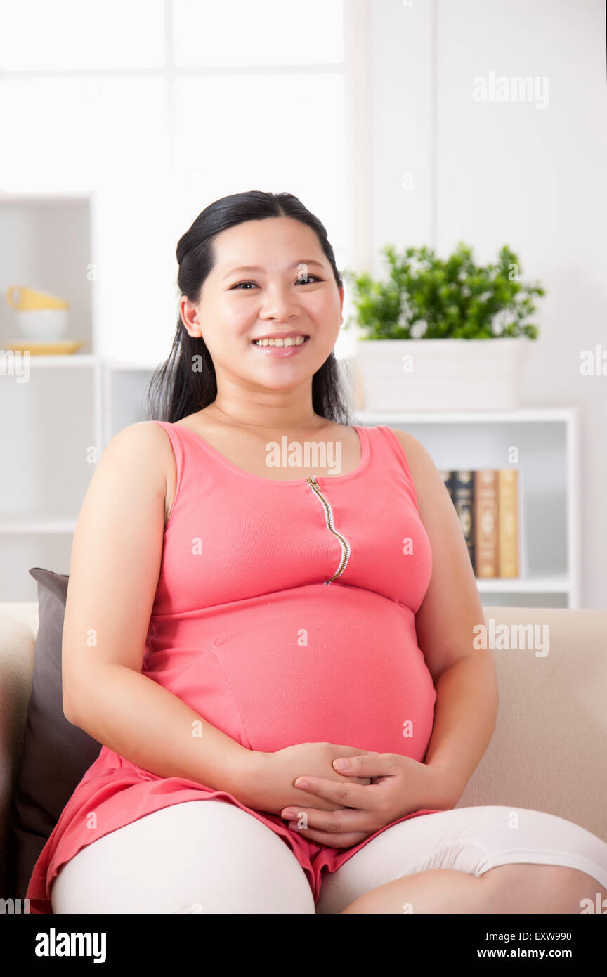 Donna incinta sorridente alla telecamera con le mani sul ventre, Foto Stock