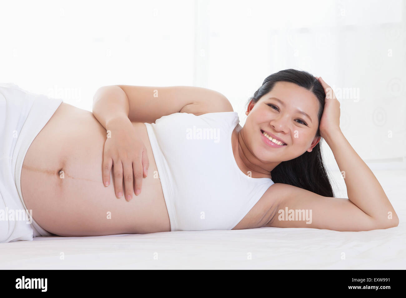 Donna incinta sdraiato sul lato e sorridente alla telecamera, Foto Stock