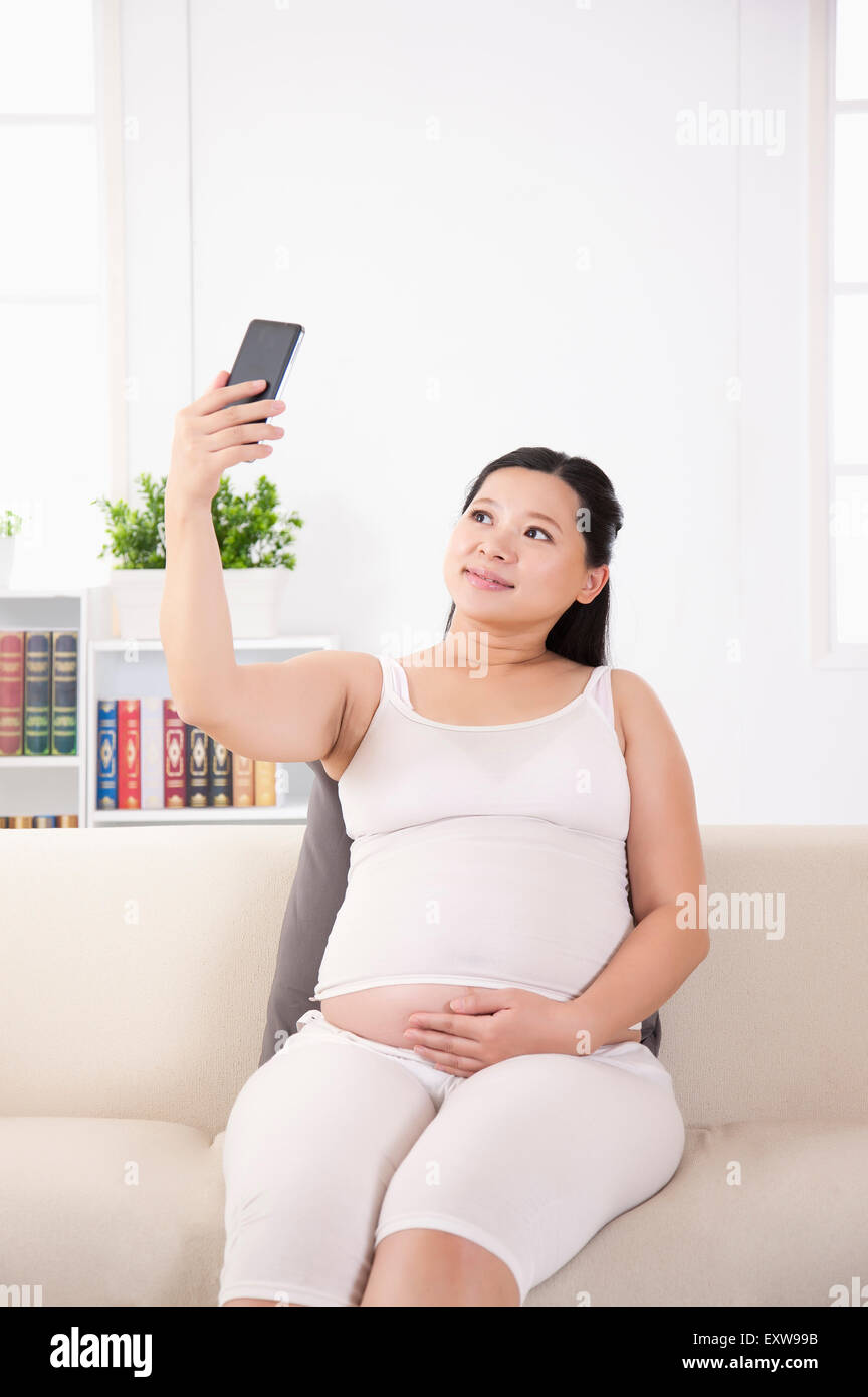 Donna incinta tenendo il telefono cellulare e di scattare la foto, Foto Stock