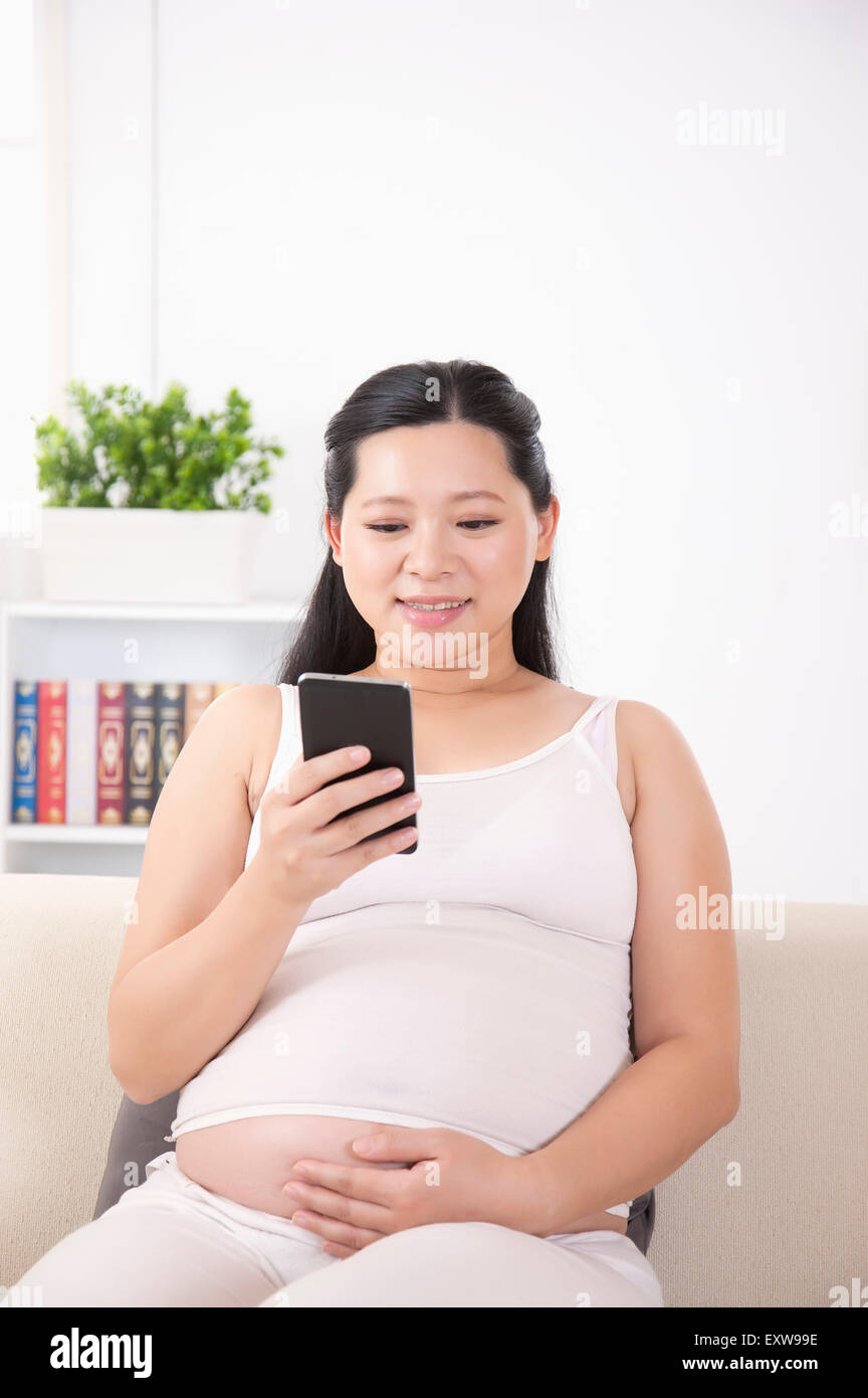 Donna incinta guardando il telefono cellulare con un sorriso, Foto Stock