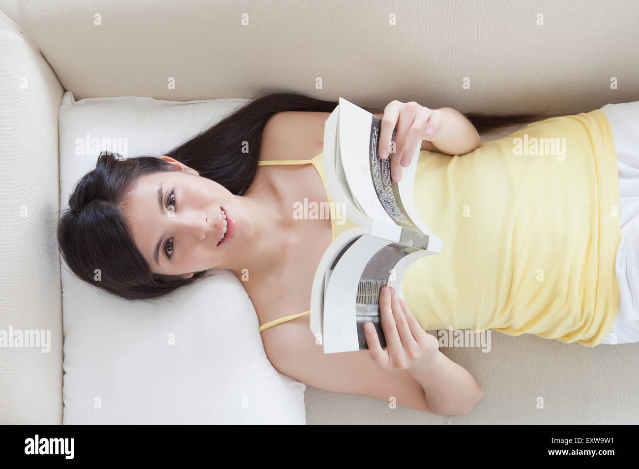 Giovane donna sdraiata e in possesso di un libro, Foto Stock