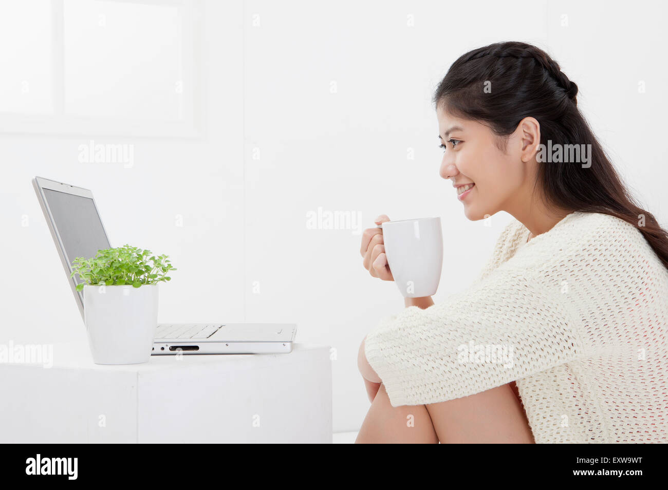 Giovane donna in possesso di una tazza di caffè e guardando il laptop con un sorriso, Foto Stock