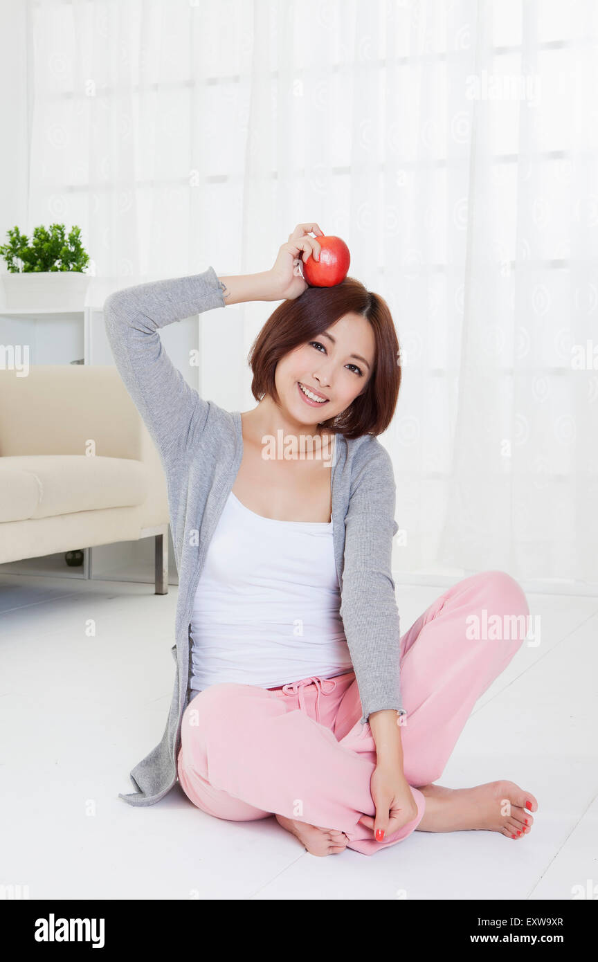 Giovane donna seduta sul pavimento e tenendo un apple, Foto Stock