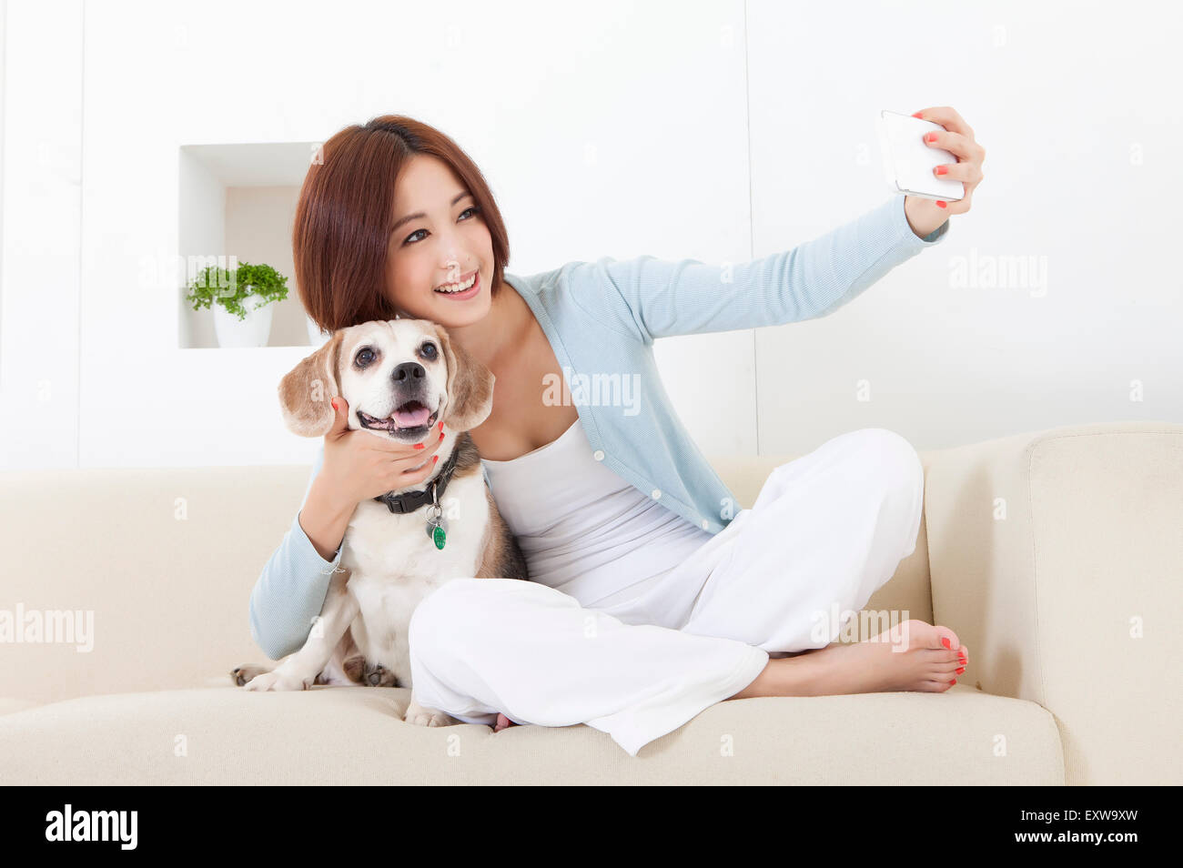 Giovane donna tenendo il telefono cellulare e abbracciando il suo cane, Foto Stock