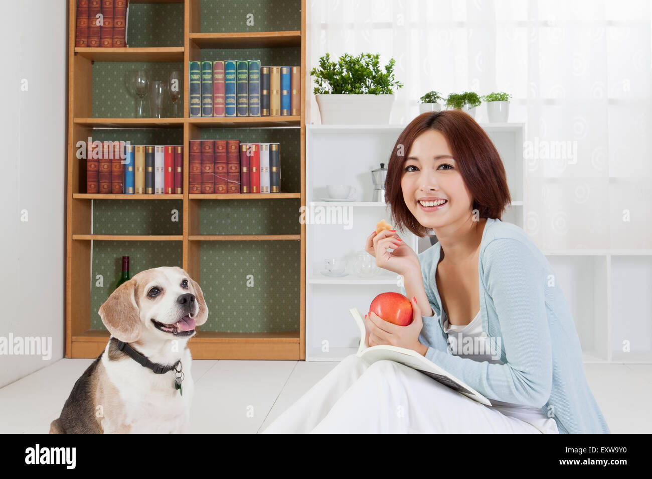 Giovane donna seduta con il suo cane e foratura di un apple con sorriso, Foto Stock