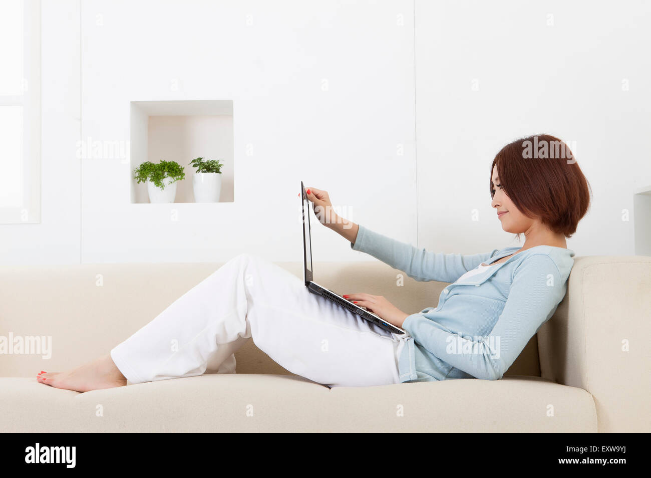 Giovane donna seduta su un divano e utilizzando laptop, Foto Stock