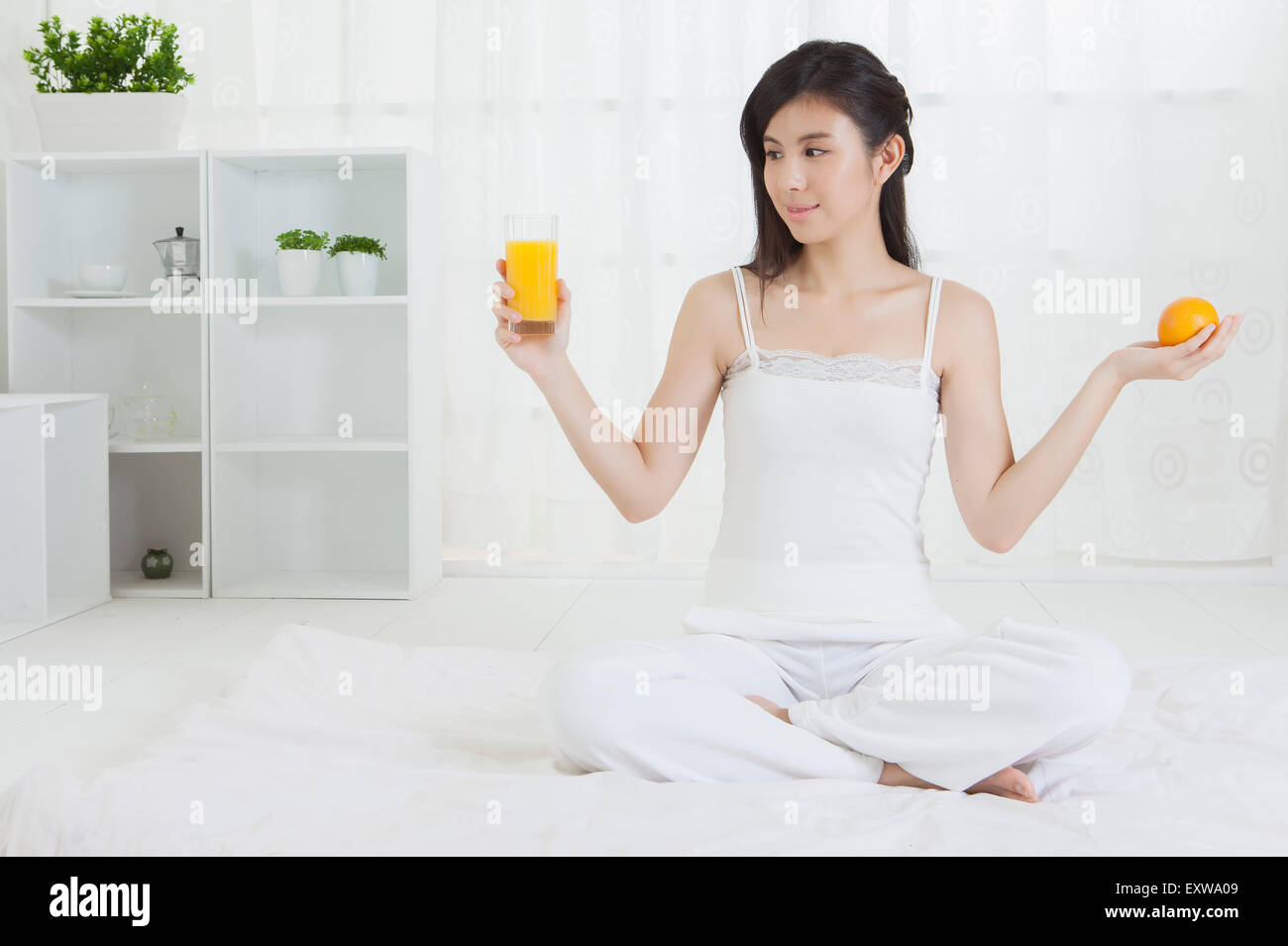 Giovane donna con in mano un bicchiere di succo di arancia e guardando lontano, Foto Stock
