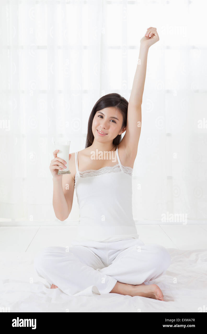 Giovane donna seduta e tenendo un bicchiere di latte, Foto Stock