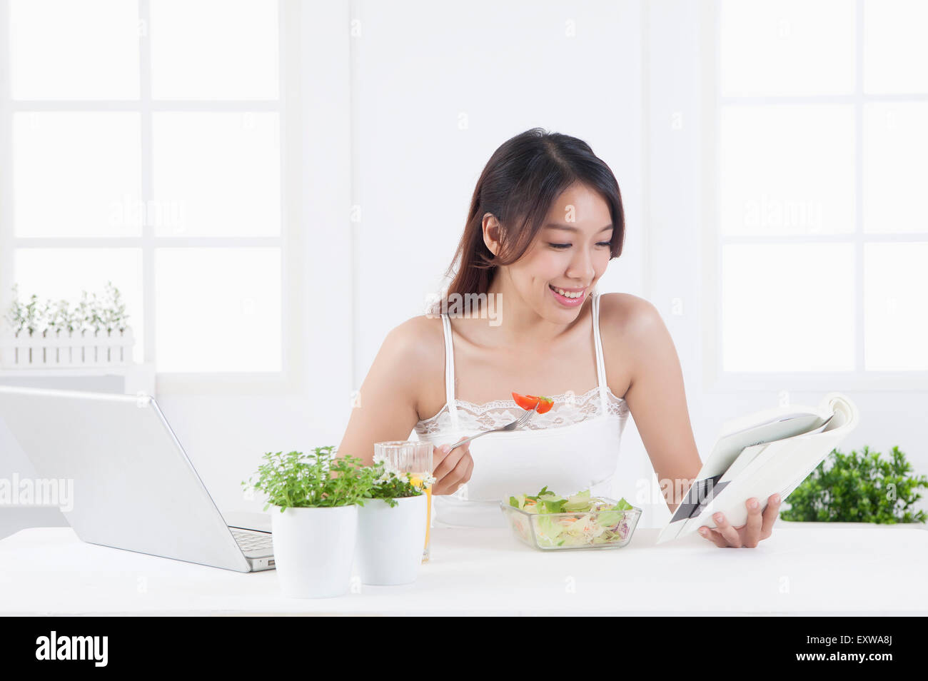 Giovane donna mangiare saland e la lettura di un libro, Foto Stock