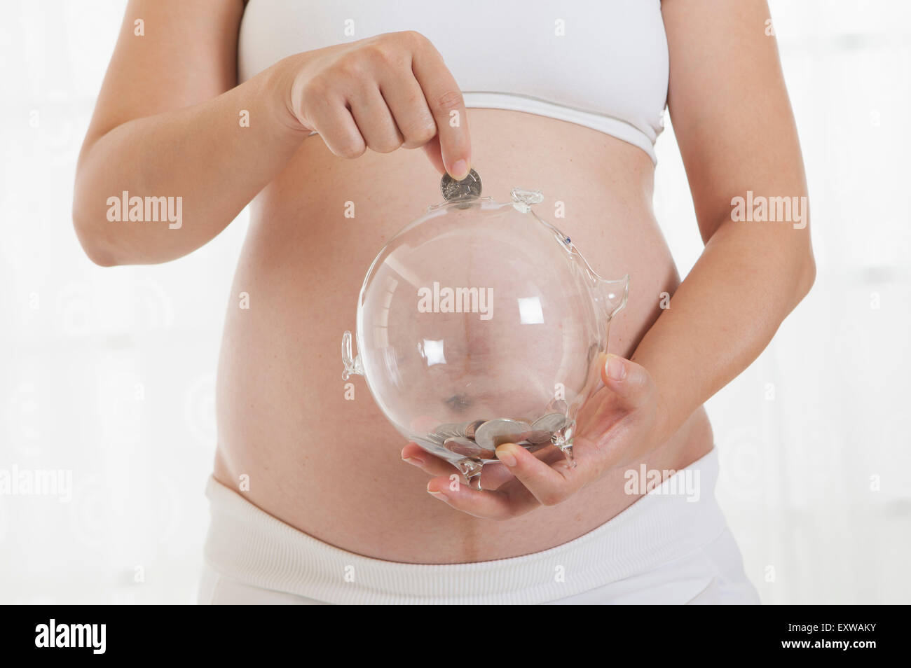 Donna incinta di mettere una moneta nella moneta banca, Foto Stock