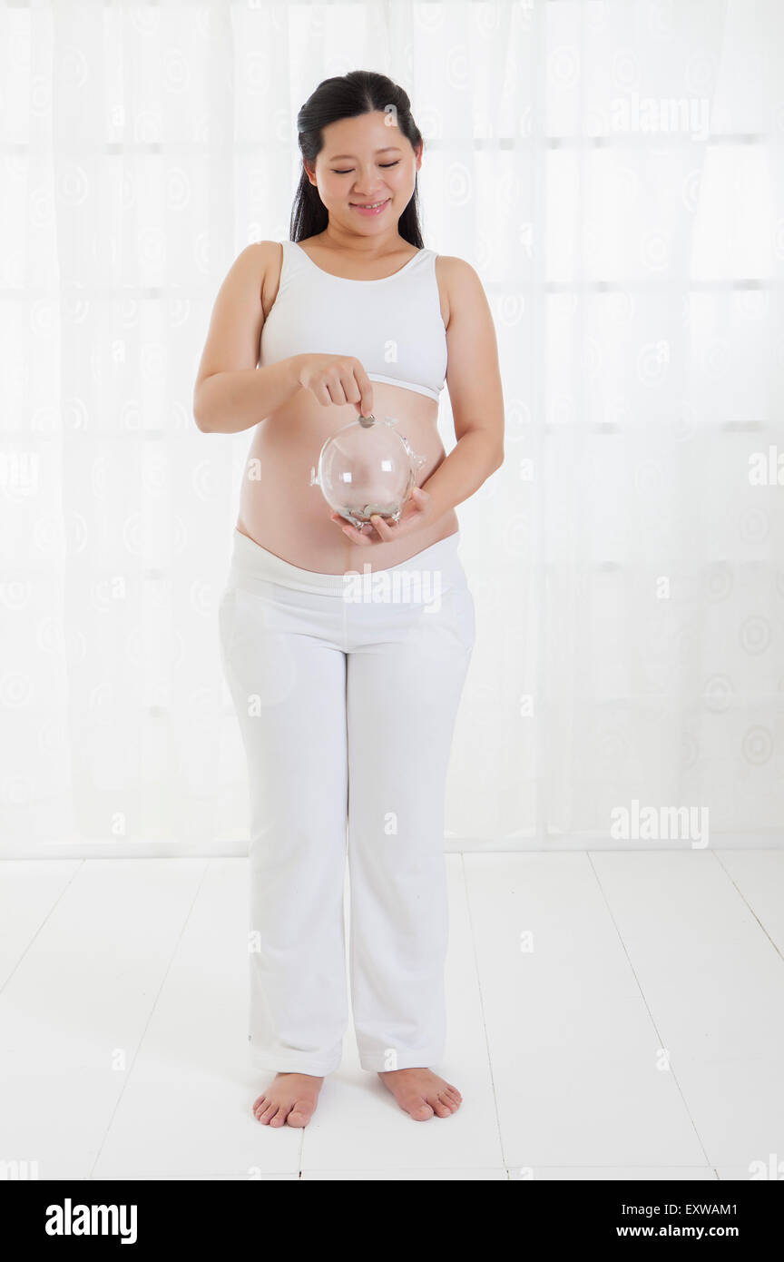Donna incinta di mettere una moneta nella moneta banca, Foto Stock