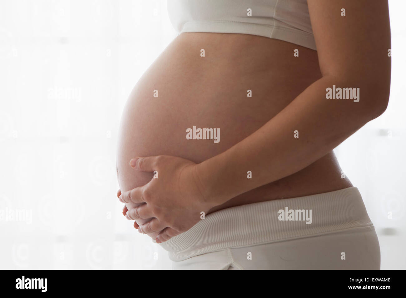 Donna incinta in piedi con le mani sul ventre, Foto Stock