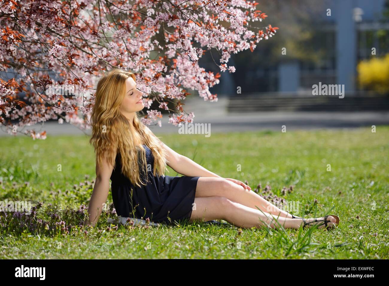 Giovane donna seduta sul prato in posizione di parcheggio Foto Stock