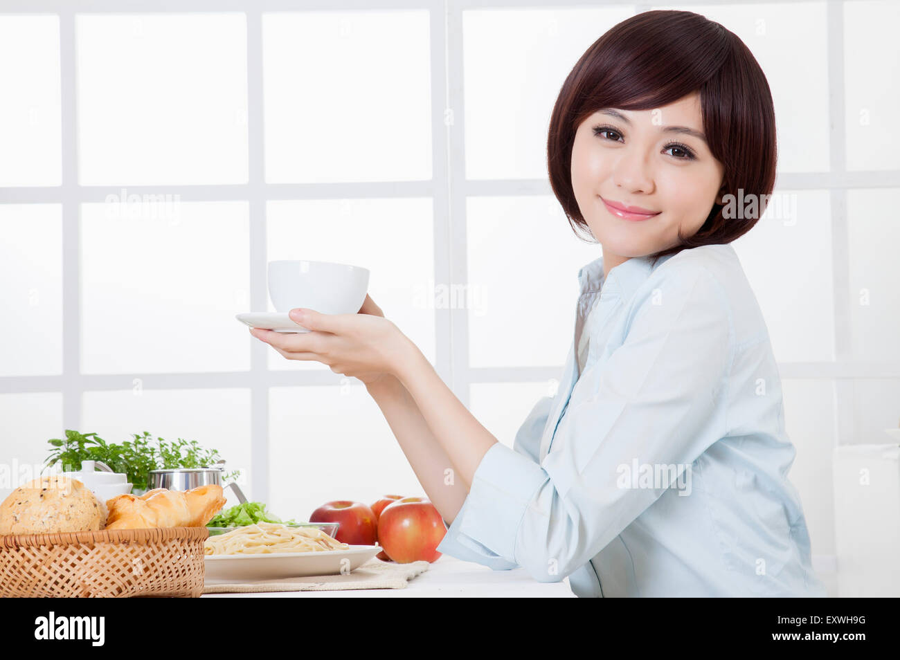 Giovane donna tenendo una tazza e sorridente alla telecamera, Foto Stock