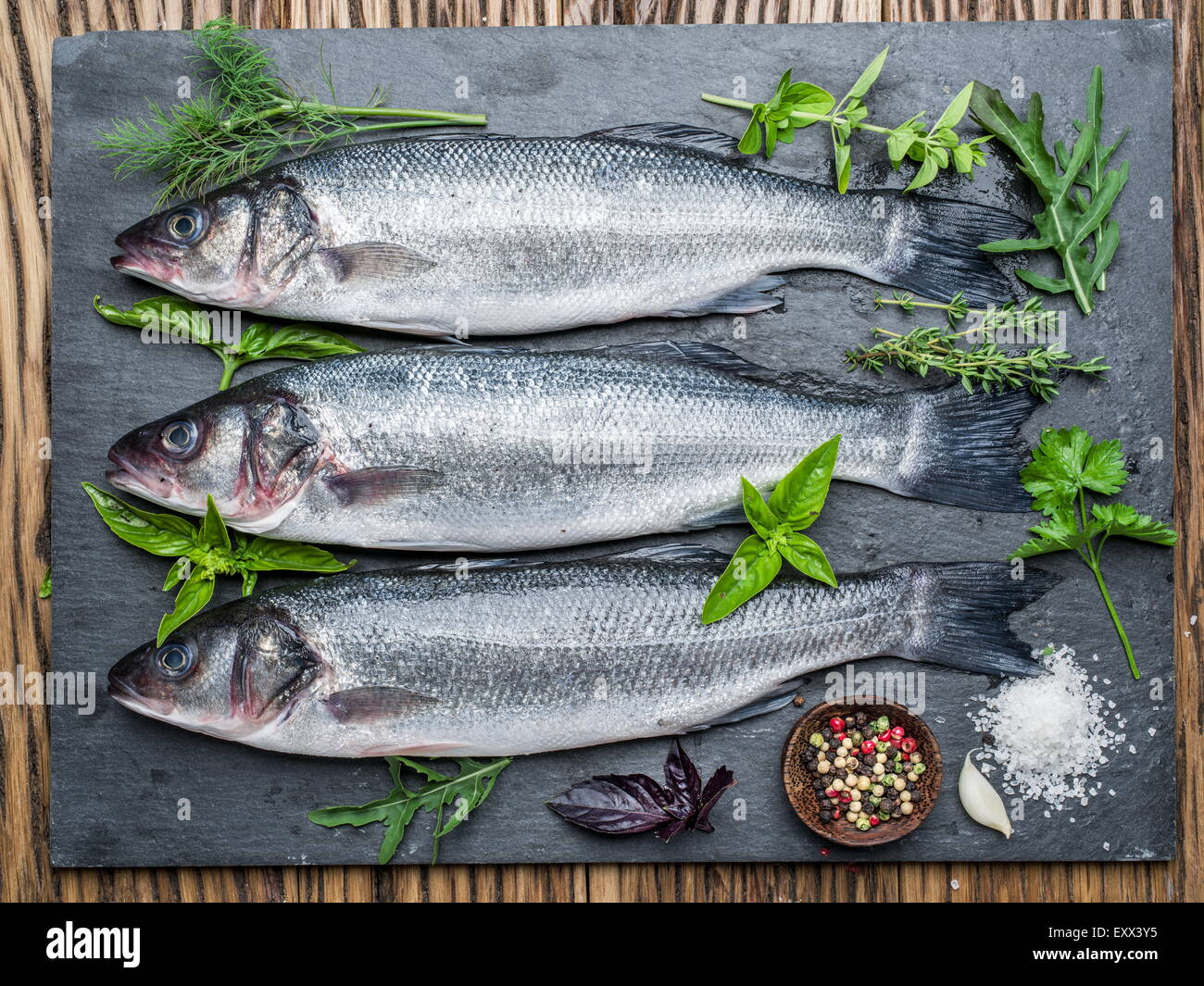 Tre pesci - sea bass su una scheda di grafite con erbe e spezie. Foto Stock