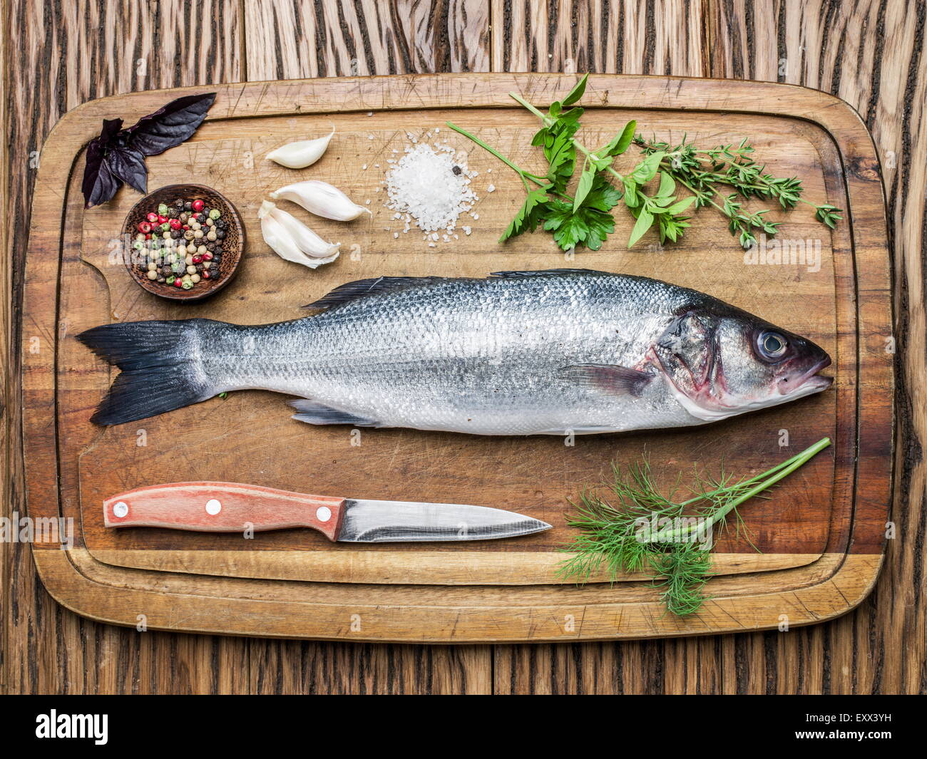 Pesce - branzino su una tavola di legno con le spezie e le erbe. Foto Stock