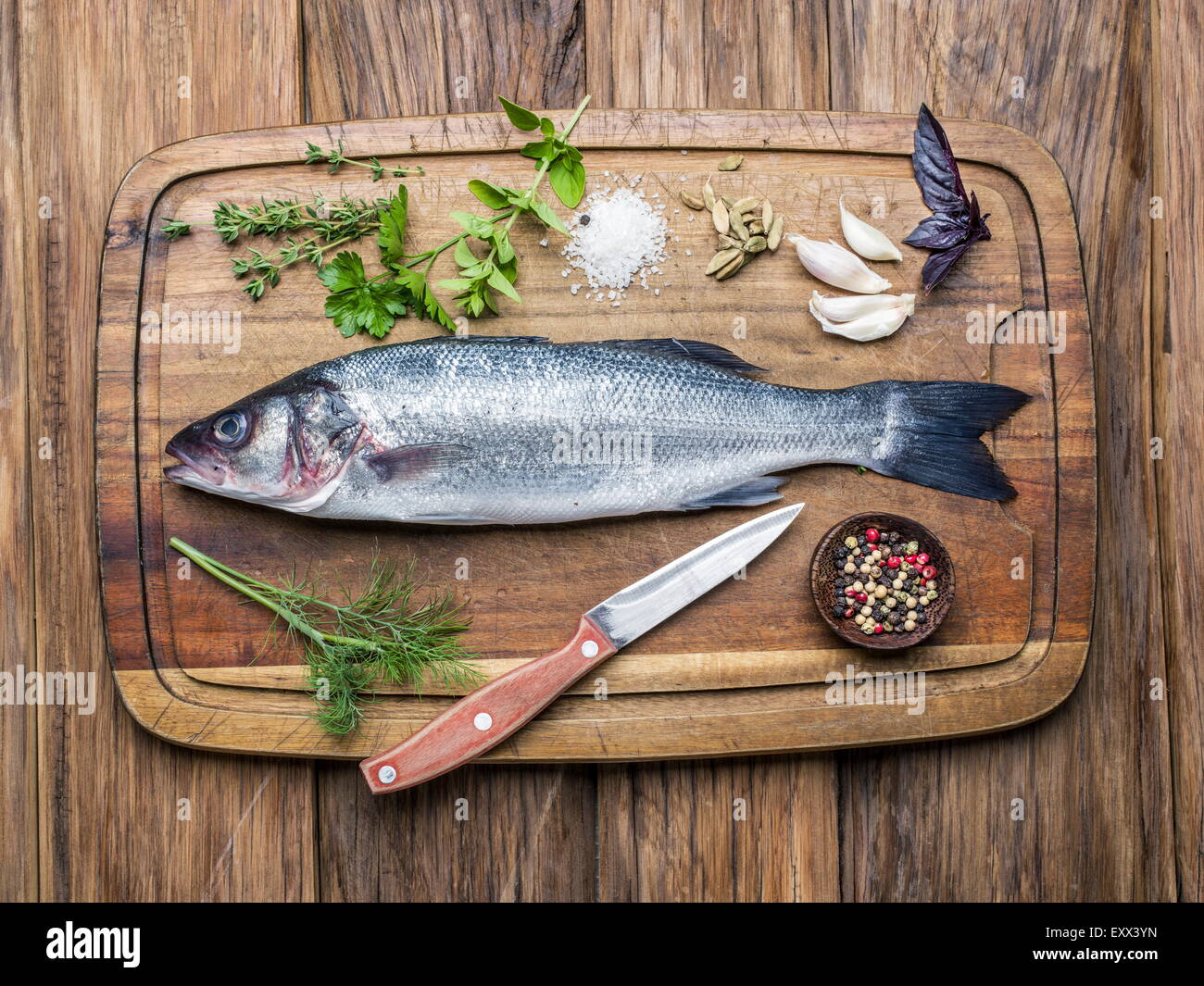 Pesce - branzino su una tavola di legno con le spezie e le erbe. Foto Stock