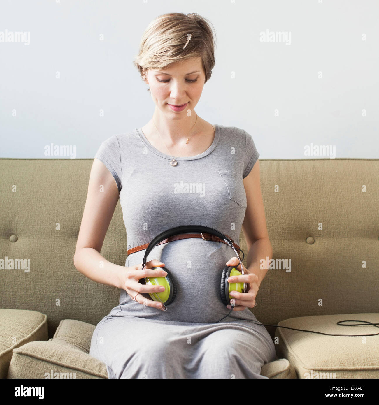 Donna incinta partecipazione delle cuffie su addome Foto Stock