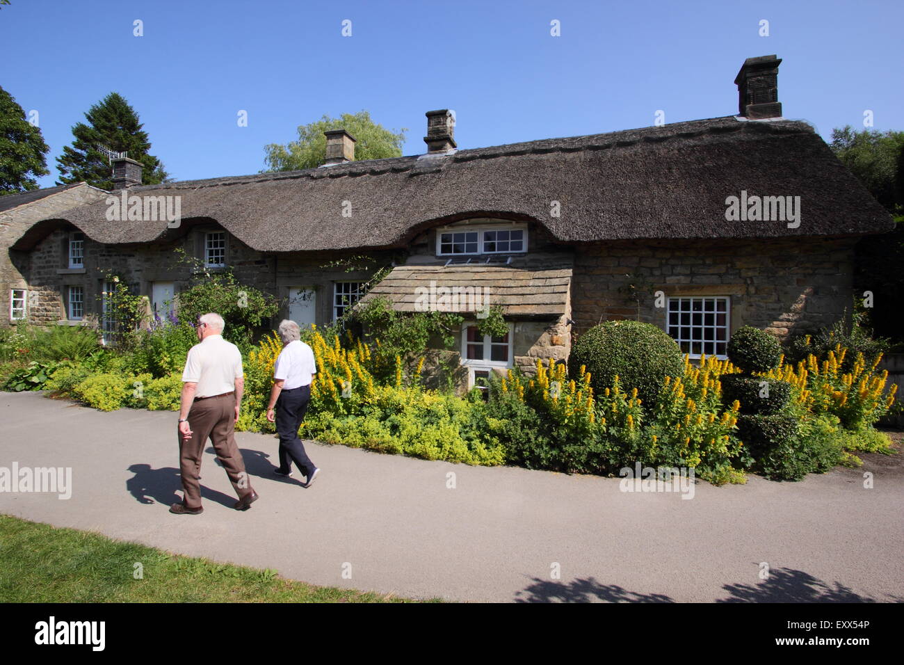 Un tman e donna passi da un tradizionale britannica cottage con il tetto di paglia nella campagna inglese, Peak District Derbyshire Inghilterra Foto Stock