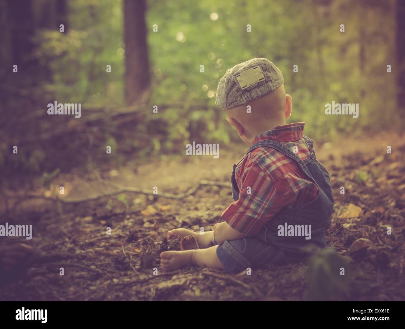 Bambino seduto nella foresta a fine estate. Ragazzo fotografato da dietro Foto Stock