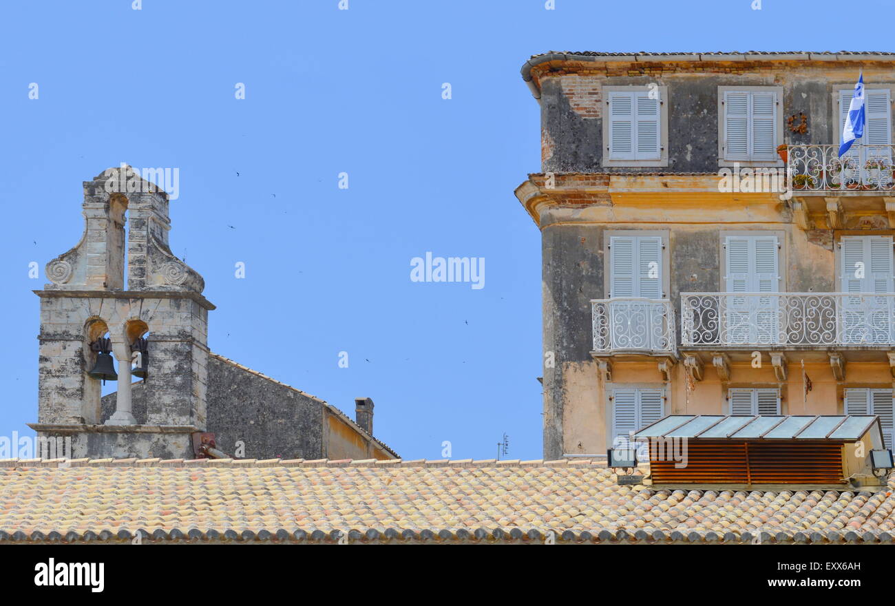 Vecchia chiesa greca avanzi e una vecchia casa con bandiera greca sventolare contro di cielo blu chiaro Foto Stock