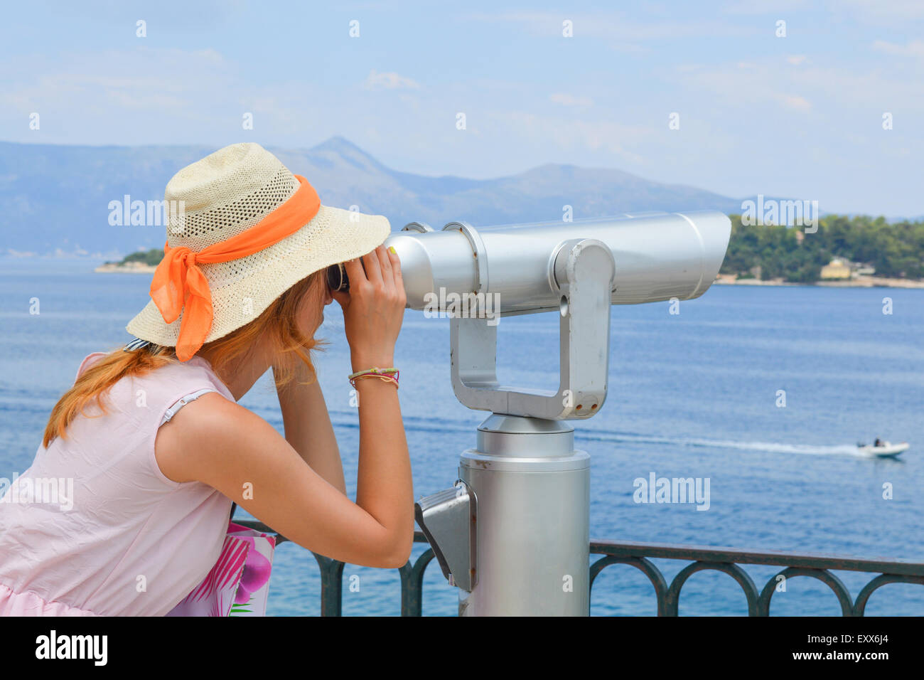 Ragazza giovane guardando attraverso il binocolo pubblica al mare indossando cappello di paglia e abito rosa Foto Stock