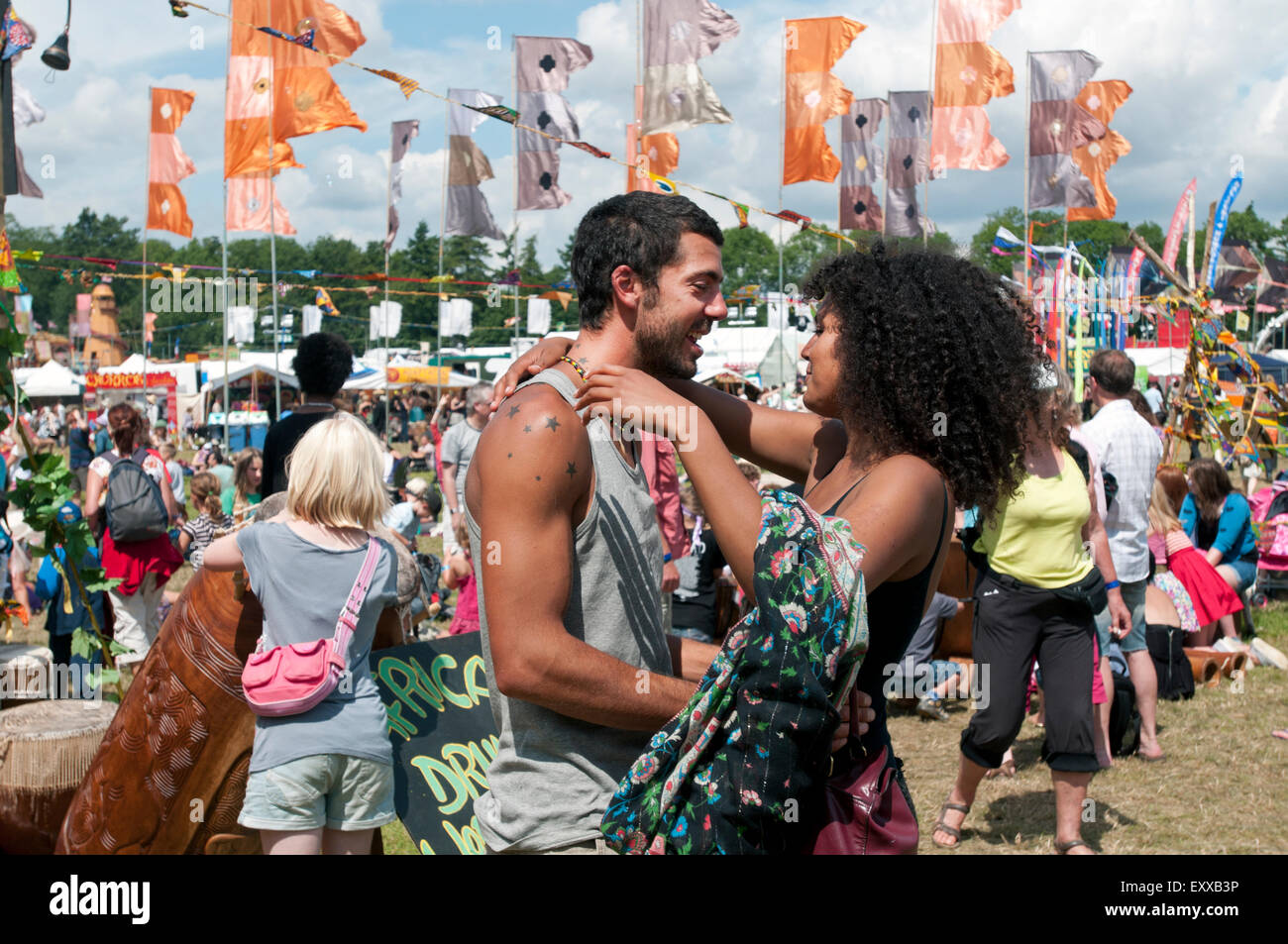 Una ragazza e Uomo in amore tenere ogni altro in un abbraccio fra la folla di persone e di bandiere del mondo WOMAD festival di musica Foto Stock