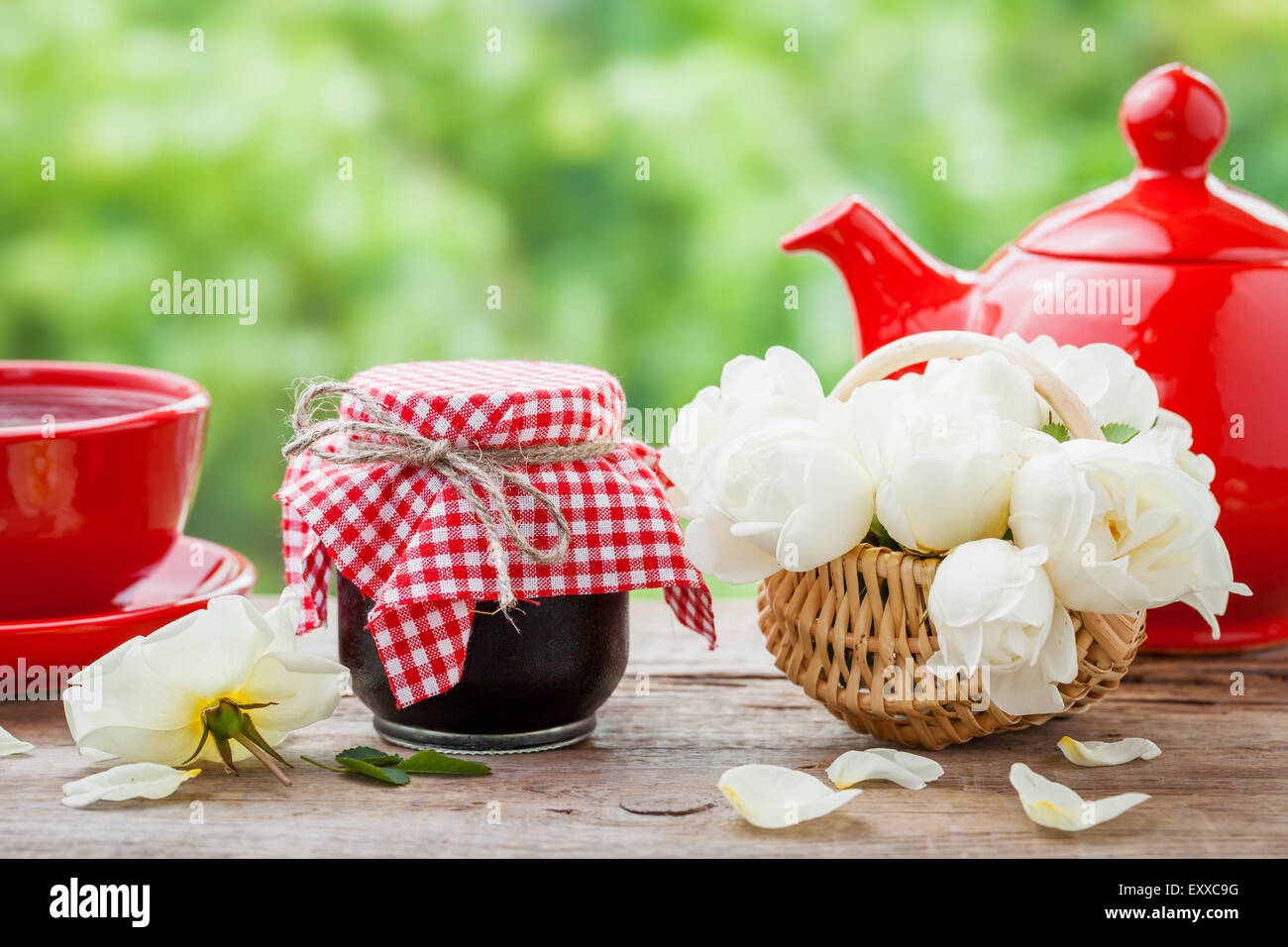 Teiera rosso, vasi di marmellata, cesto con mazzo di rose e la tazza da tè. Foto Stock