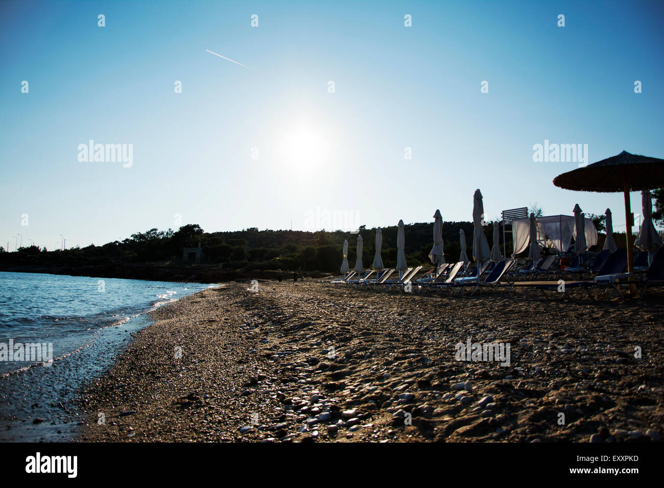 E sabbiosa spiaggia di ciottoli con sedie a sdraio e ombrelloni al tramonto Foto Stock
